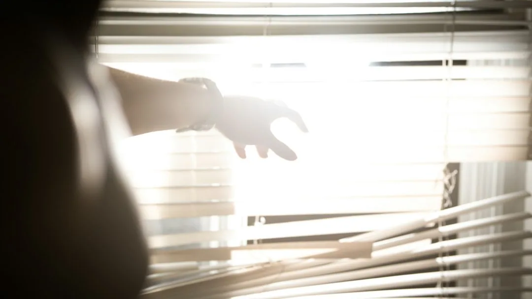 Mano en tensión ante una ventana con persianas, símbolo del conflicto al despedir un trabajador por robo que asesora Barcelona Laboral